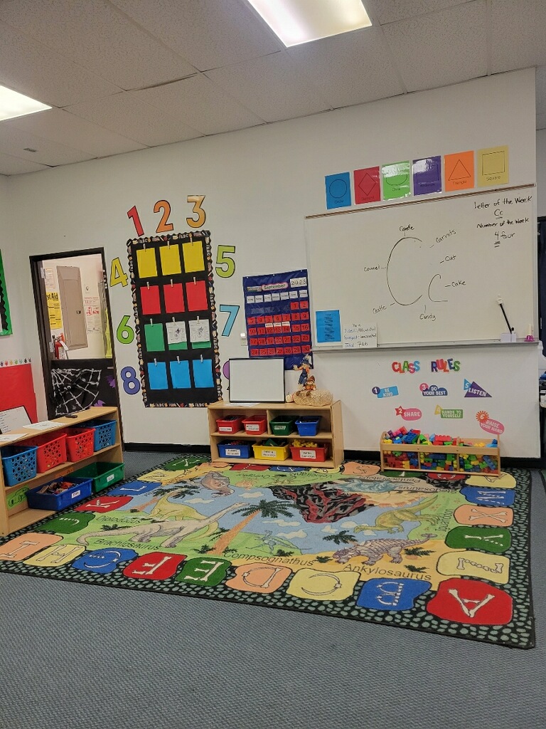 Front of a children's classroom with an alphabet rug, whiteboard, and posters of numbers and class rules