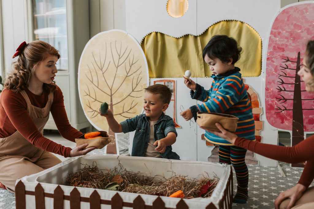 Two toddlers playing in a box with grass inside it with their teacher